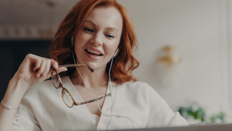 Mulher ruiva confiante e satisfeita concentrada no laptop, assiste vídeo ou filme no laptop, desfruta de observa portfólio profissional online, ela é amigável, segura óculos transparentes,